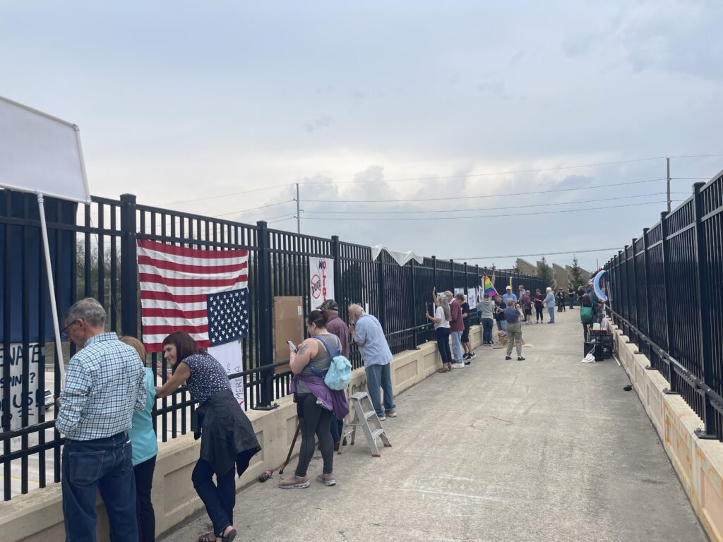 A large group of protesters display signs and flags at an overpass.