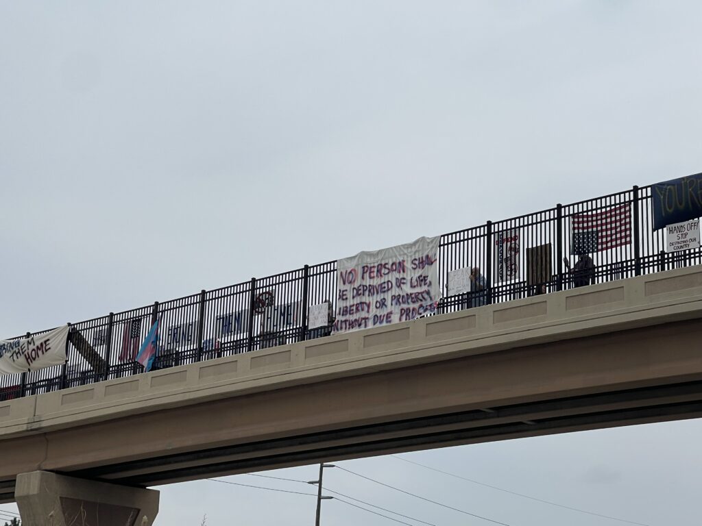 A large group of protesters display signs and flags at an overpass.