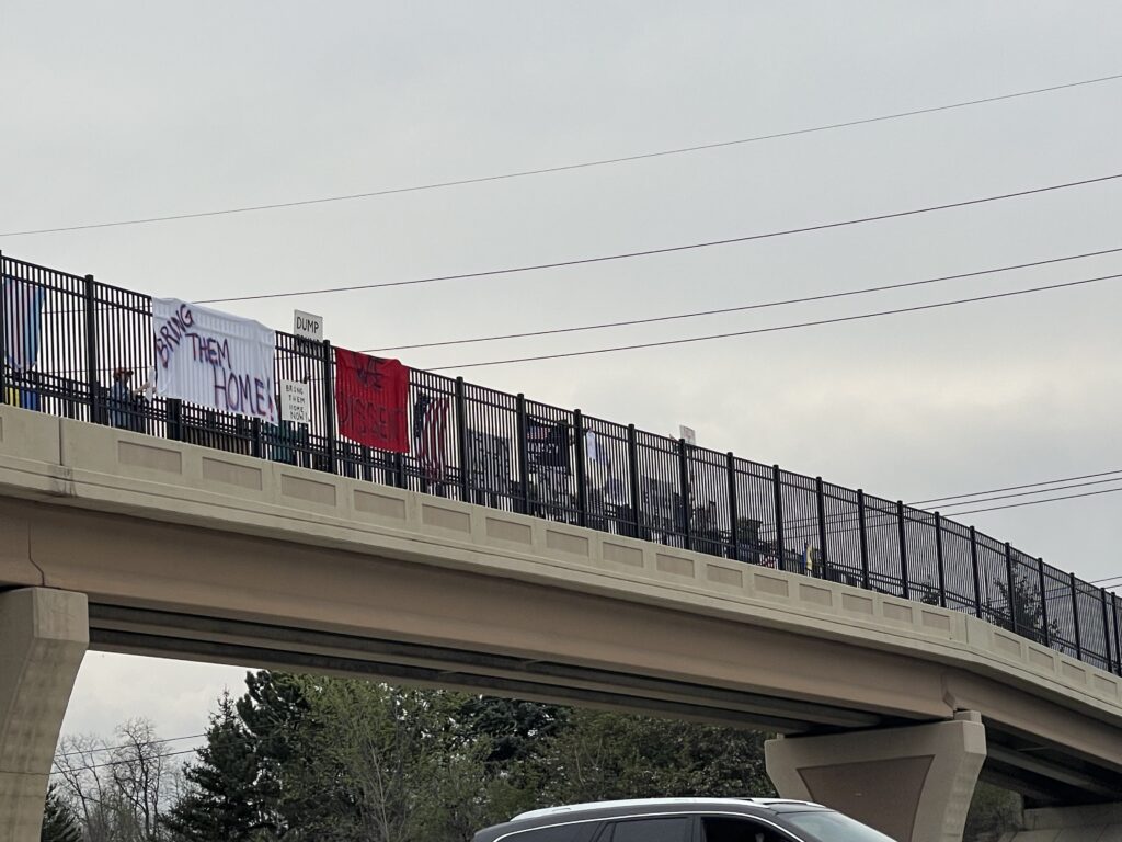 A large group of protesters display signs and flags at an overpass.