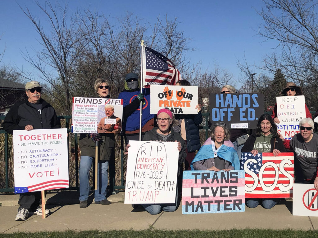 A group of protesters from Western Wayne Indivisible holding a variety of signs supporting American democracy.