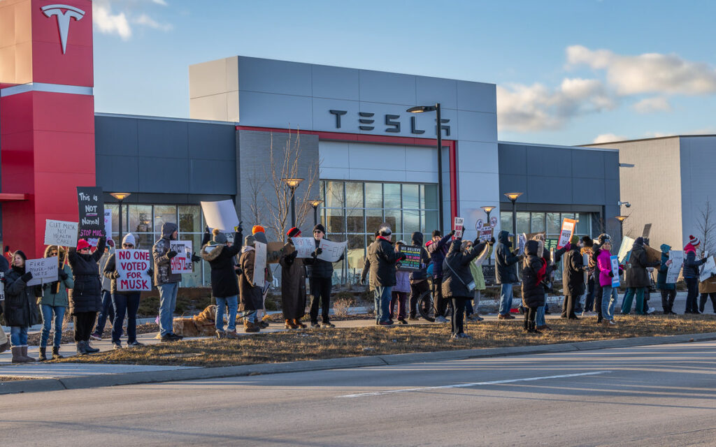 A crowd of protesters outside of a Tesla dealership