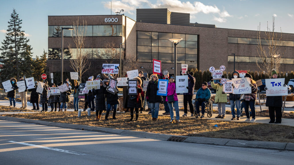 A crowd of protesters outside of a Tesla dealership